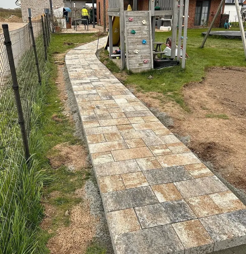 Gartenweg aus Betonpflaster entlang eines Zauns, daneben ein Spielturm